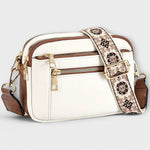 White small crossbody bag with flap front, front zipper, and floral patterned strap.