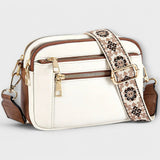 White small crossbody bag with flap front, front zipper, and floral patterned strap.