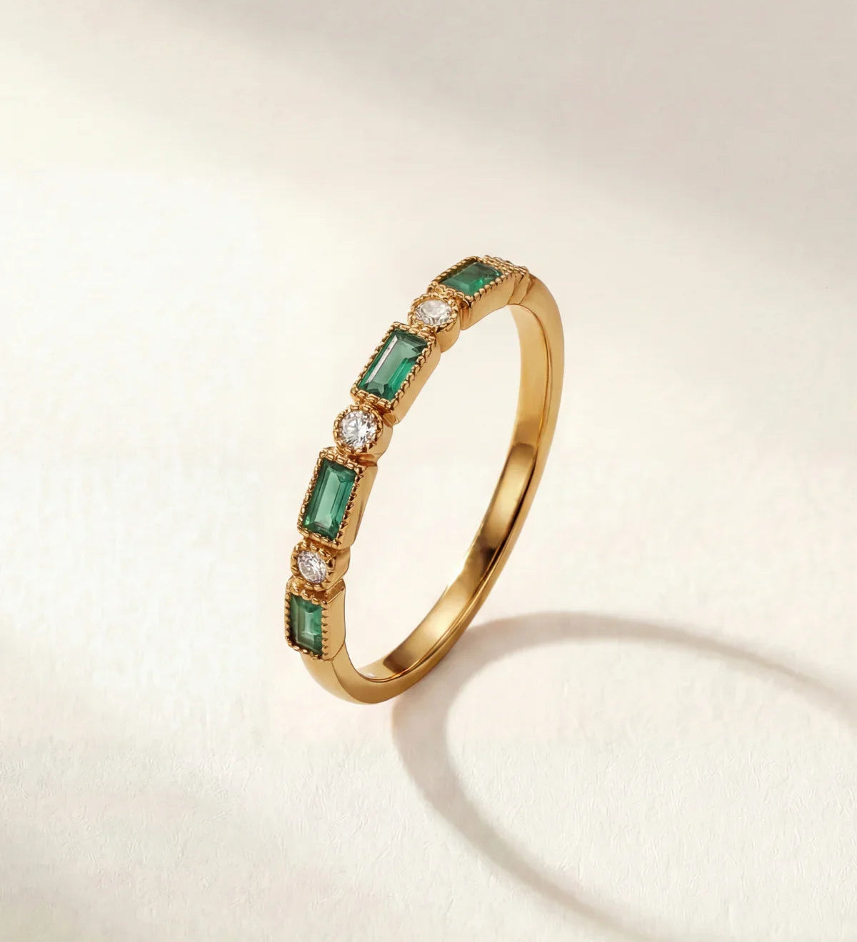 Gold ring with green rectangular stones and small clear accents on a thin band