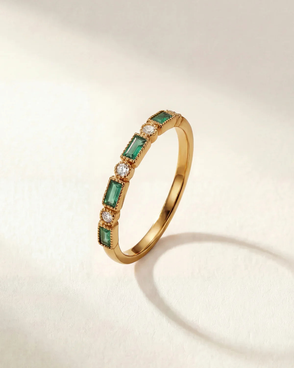 Gold ring with green rectangular stones and small clear accents on a thin band