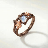 Bronze branch-effect ring with oval opalescent blue center and clear sparkle stones