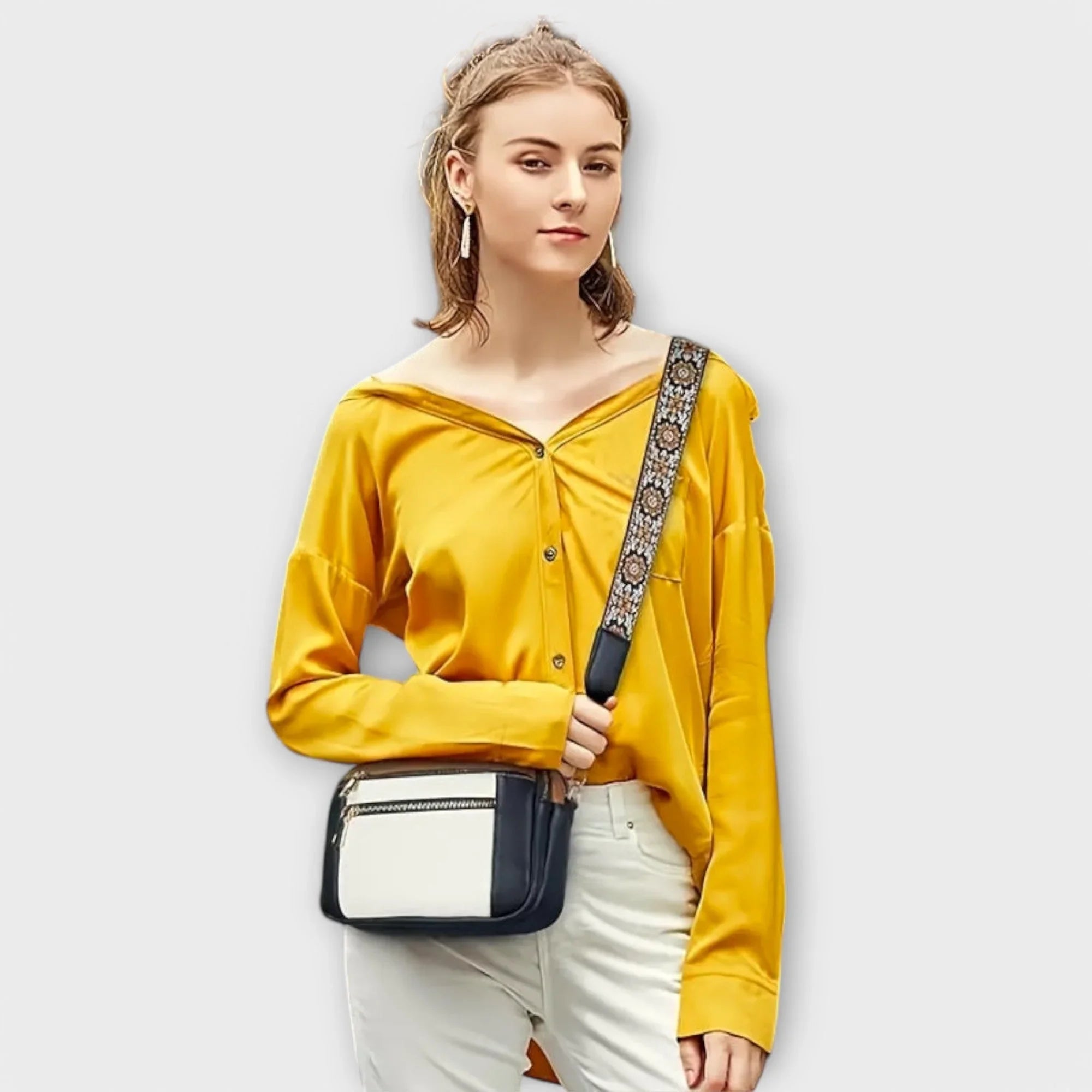 Small crossbody bag with white front panel and floral patterned strap, worn across chest.