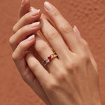 Wide gold band ring with multicolored gemstone stones on finger