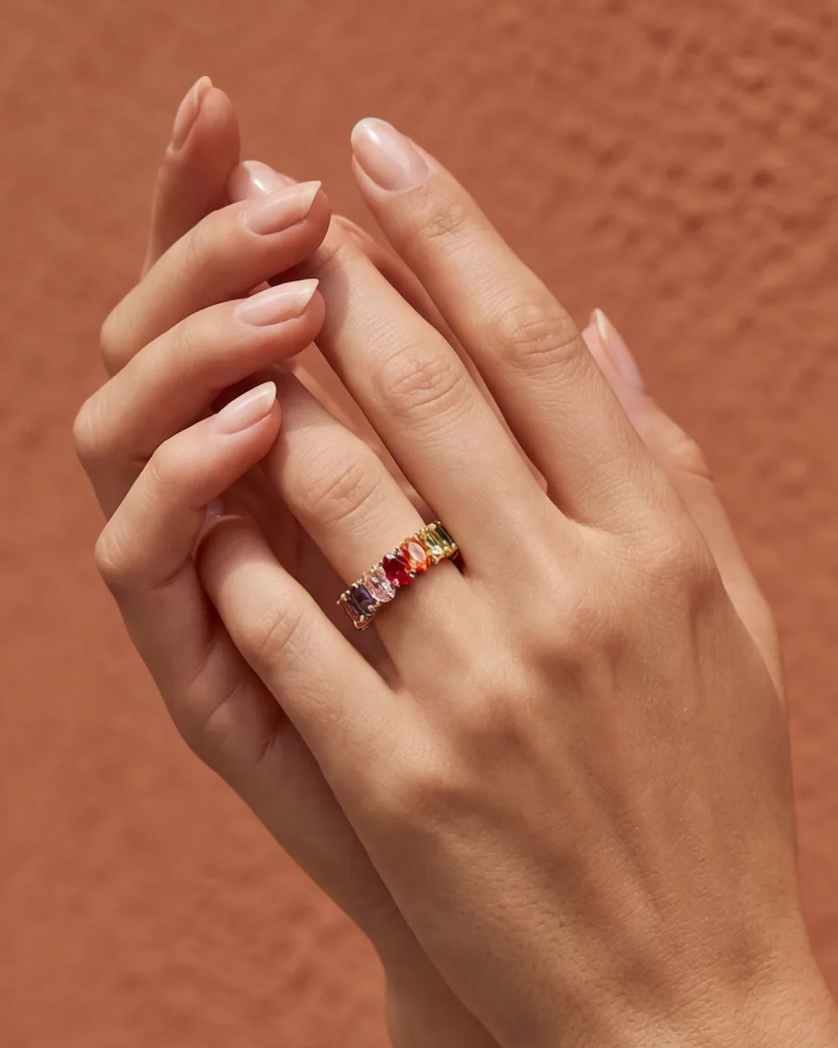 Wide gold band ring with multicolored gemstone stones on finger