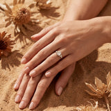 Gold ring with clear cluster stone on finger, hands resting on sand