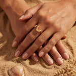 Gold wavy ring on finger with manicured nails on sand