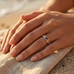 Gold ring with blue gemstones, close-up on hand on sand
