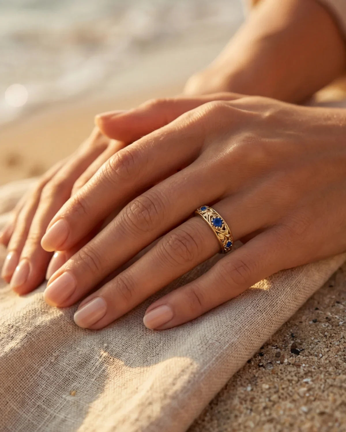 Gold ring with blue gemstones, close-up on hand on sand