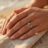 Gold ring with blue gemstones, close-up on hand on sand