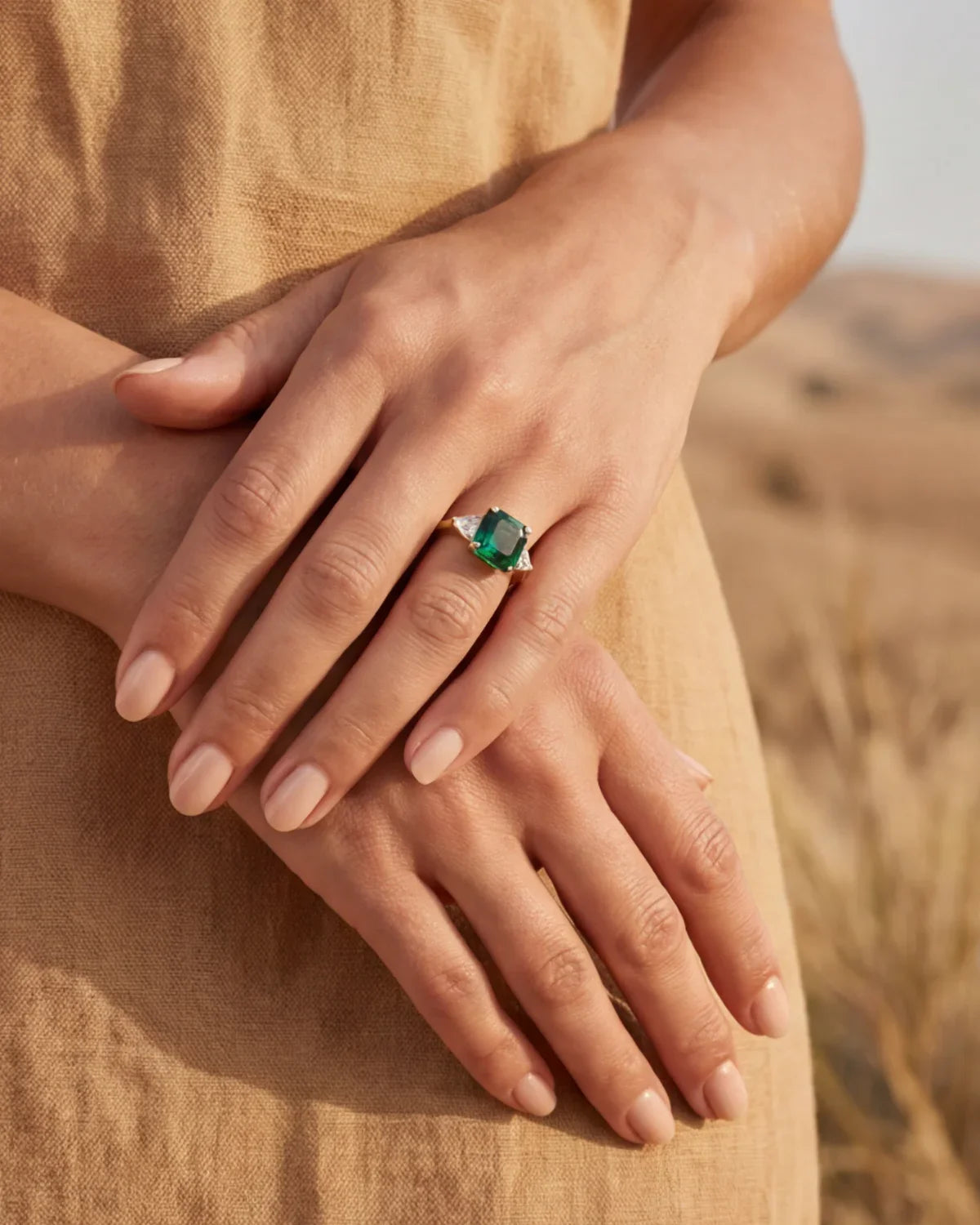 Gold ring with green stone on hand, fingers resting on beige fabric
