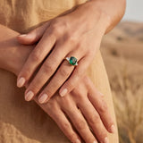 Gold ring with green stone on hand, fingers resting on beige fabric