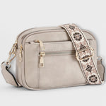 Light gray small crossbody bag with flap front, front zipper pocket, and patterned strap.