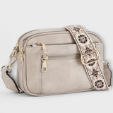 Light gray small crossbody bag with flap front, front zipper pocket, and patterned strap.