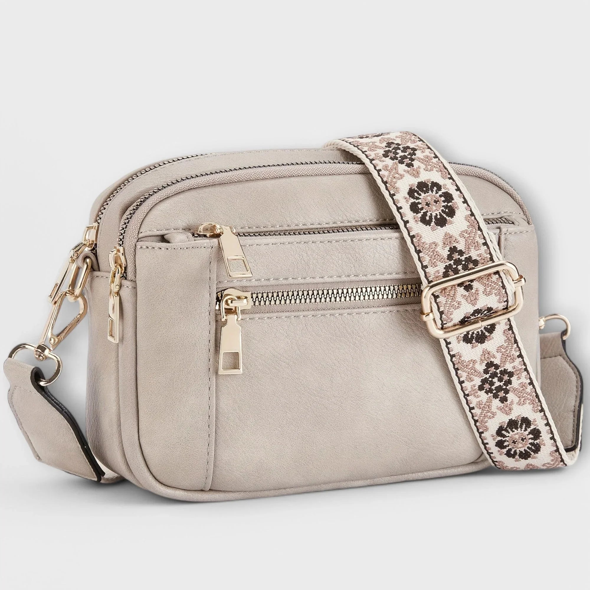 Light gray small crossbody bag with flap front, front zipper pocket, and patterned strap.