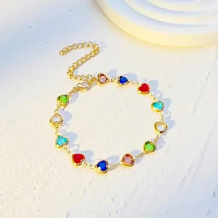 Gold-tone heart charm bracelet with colorful heart stones, chain loop flat lay
