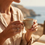 Gold ring with blue gemstones on hand holding ceramic cup