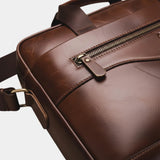 Caramel leather briefcase corner detail with metal zipper pull and crossbody strap.
