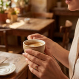 Gold band ring with multicolored stones on finger near coffee cup