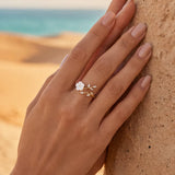 Gold-tone ring with white flower detail and clear stones near wrist