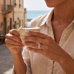 Infinity ring in gold and silver on a hand holding a coffee cup.