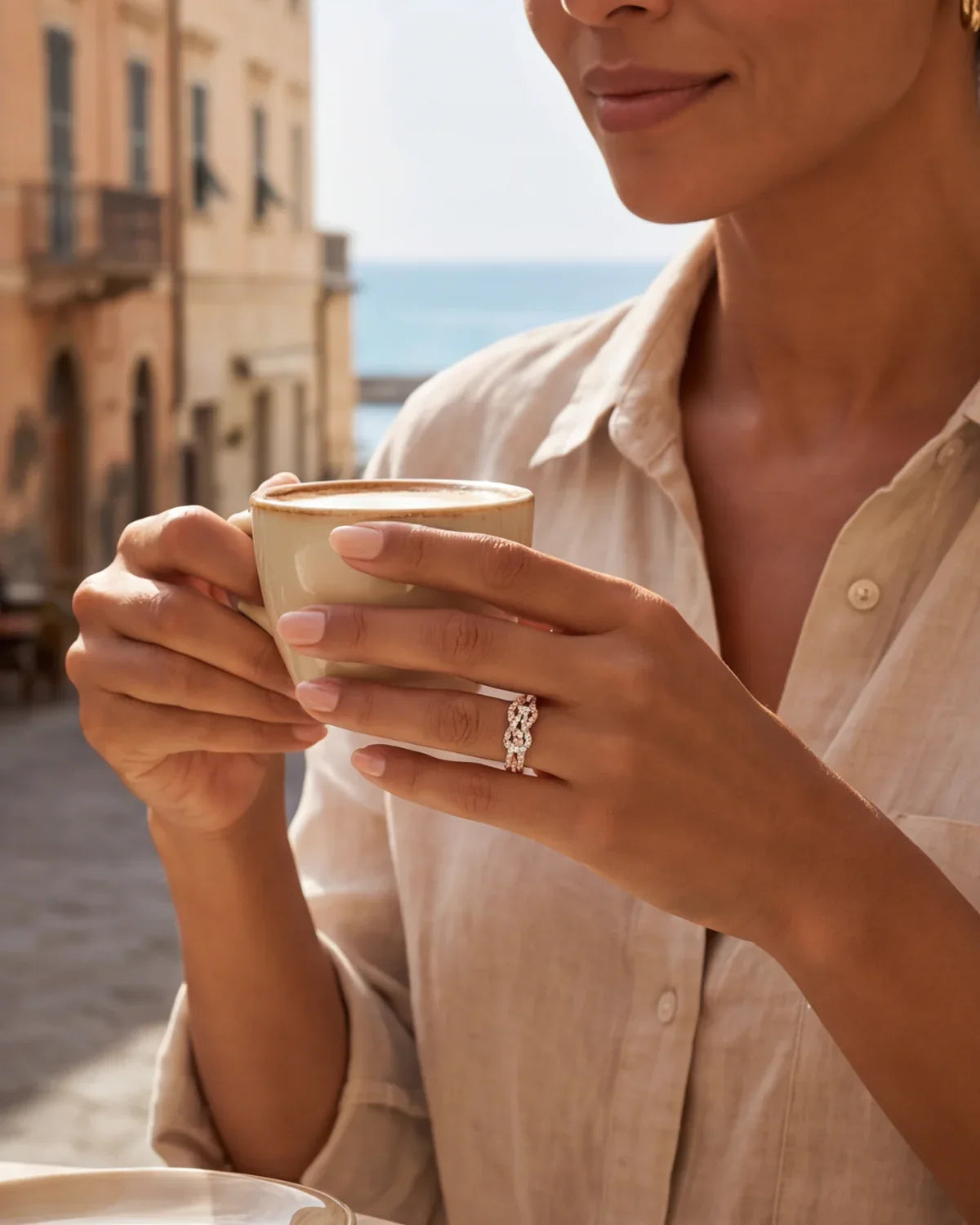Infinity ring in gold and silver on a hand holding a coffee cup.