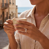 Infinity ring in gold and silver on a hand holding a coffee cup.