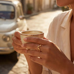 Gold wavy ring on finger holding a coffee cup