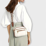 White crossbody bag with brown trim and floral patterned strap, worn on the shoulder.