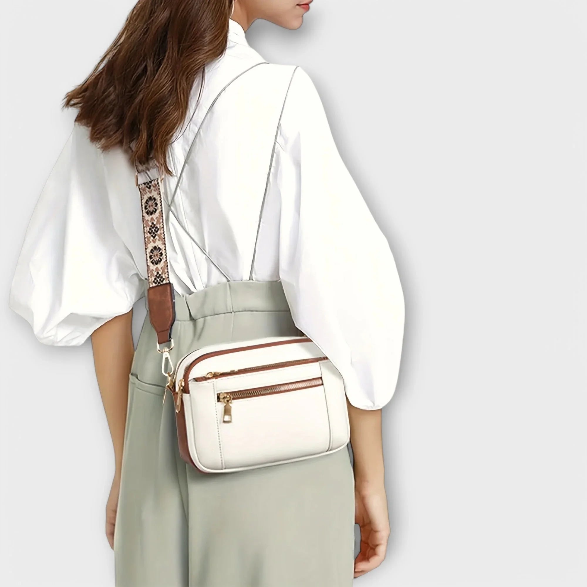White crossbody bag with brown trim and floral patterned strap, worn on the shoulder.