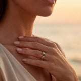 Gold ring with blue gemstones on finger, oval center setting