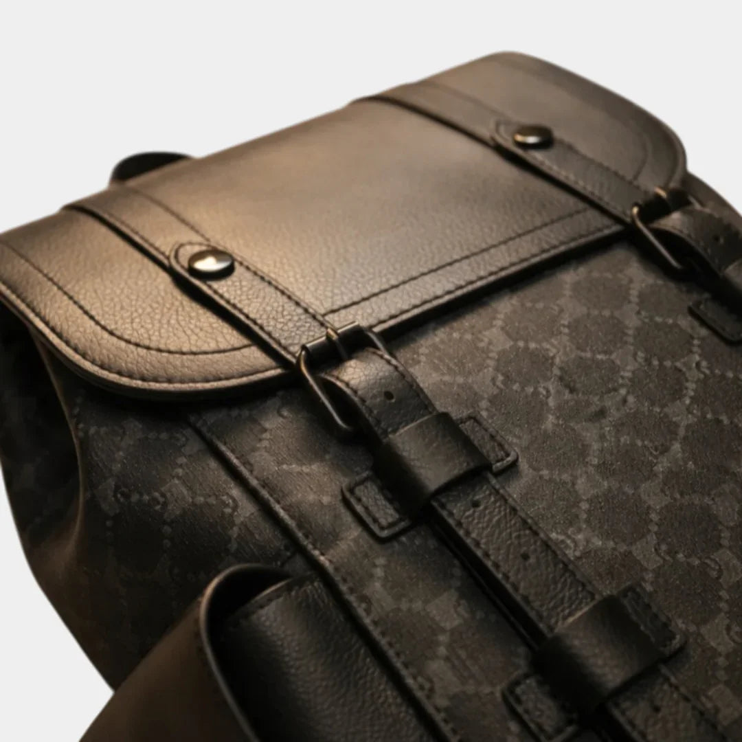 Black leather backpack close-up: textured panel, flap strap, and metal buckles