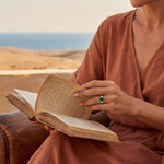 Gold ring with green stone on finger while holding an open book