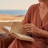 Gold ring with green stone on finger while holding an open book