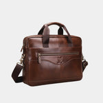 Caramel leather briefcase with front emblem, top handles, and adjustable shoulder strap.