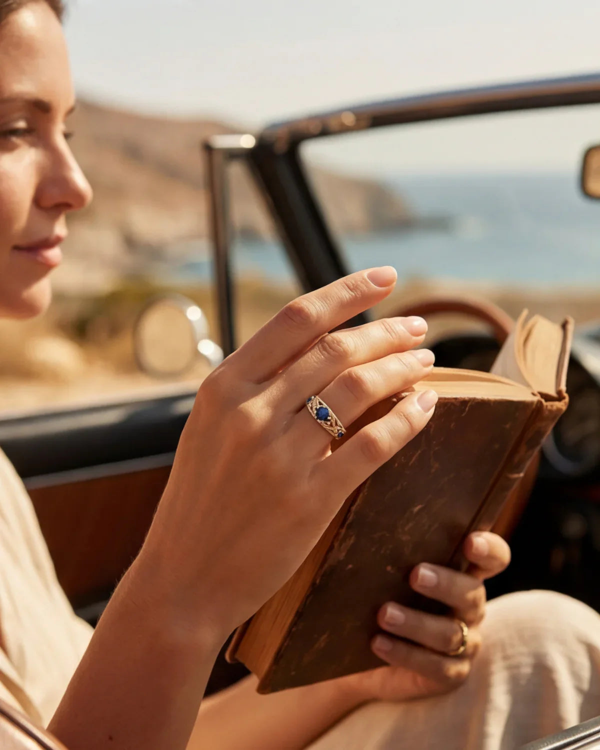 Gold ring with blue gemstones on finger near open book in car