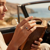 Gold ring with blue gemstones on finger near open book in car