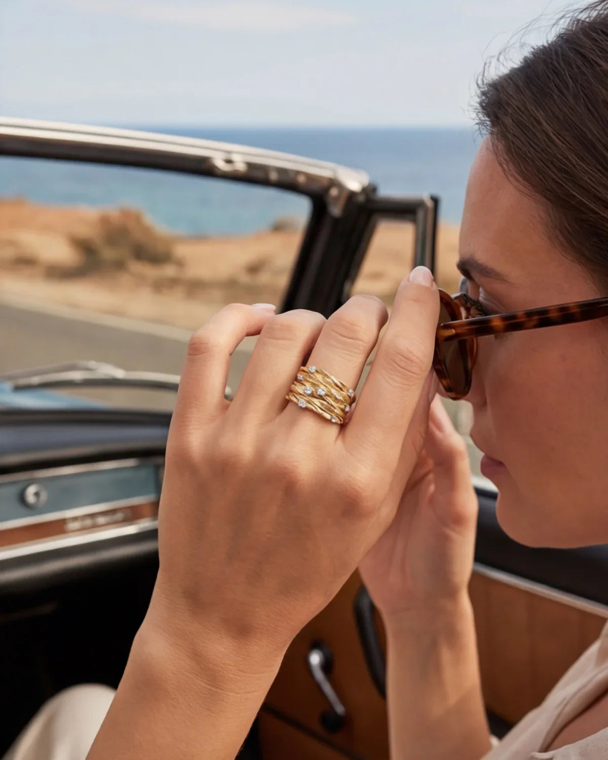Gold-tone ring worn on a hand; curved band with clear gemstone details