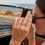 Gold-tone ring worn on a hand; curved band with clear gemstone details