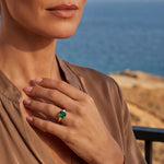 Gold ring with green square-cut stone on finger