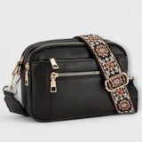 Black small crossbody bag with flap front, front zipper, and floral patterned strap.