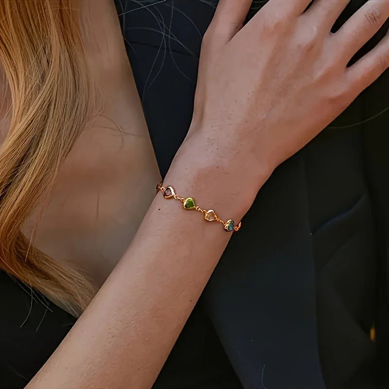 Gold-tone heart charm bracelet with small multicolor heart stones on wrist