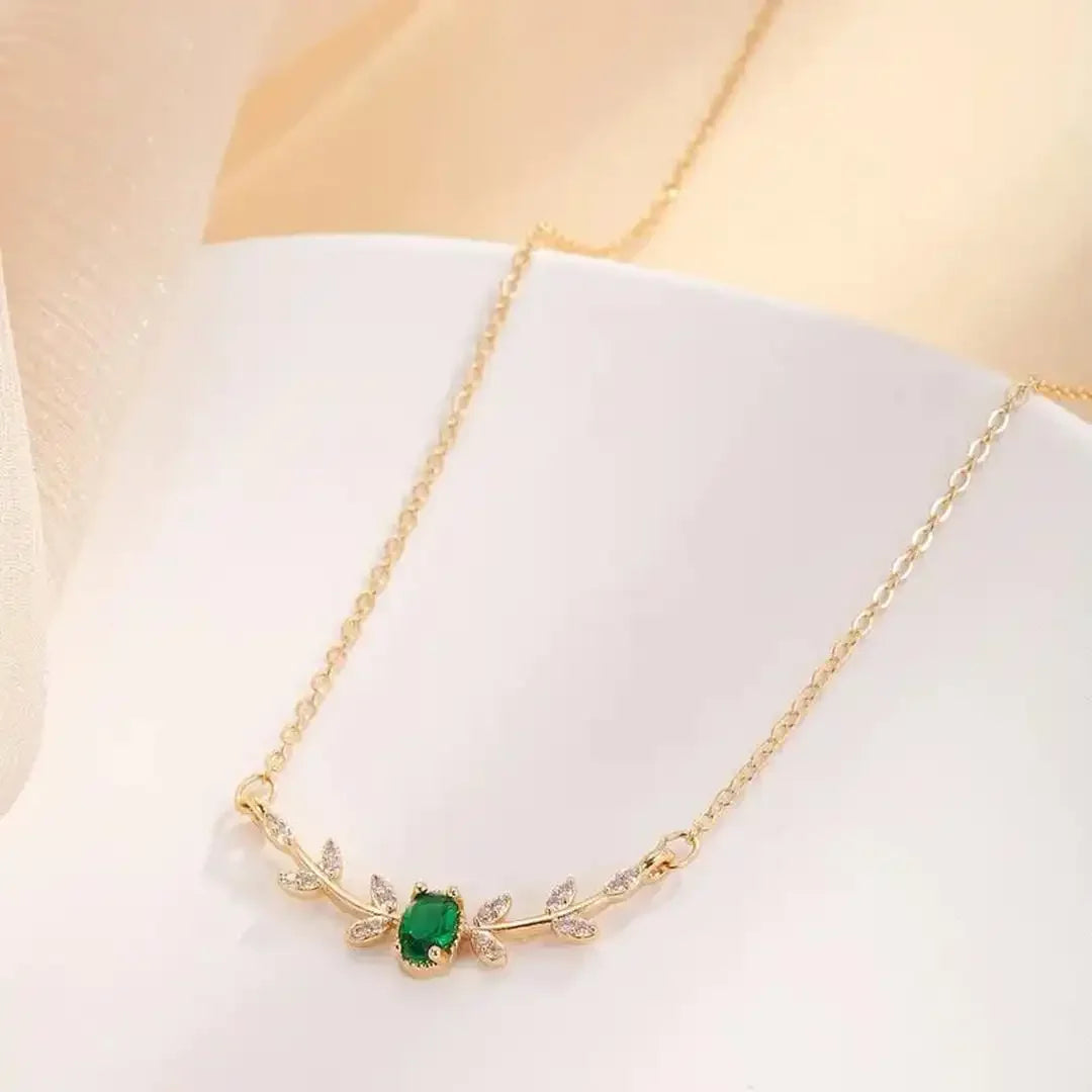 Gold pendant necklace with green leaf centerpiece and diamond-like accents