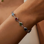 Silver-tone heart charm bracelet with dark blue, green, and red gemstone hearts