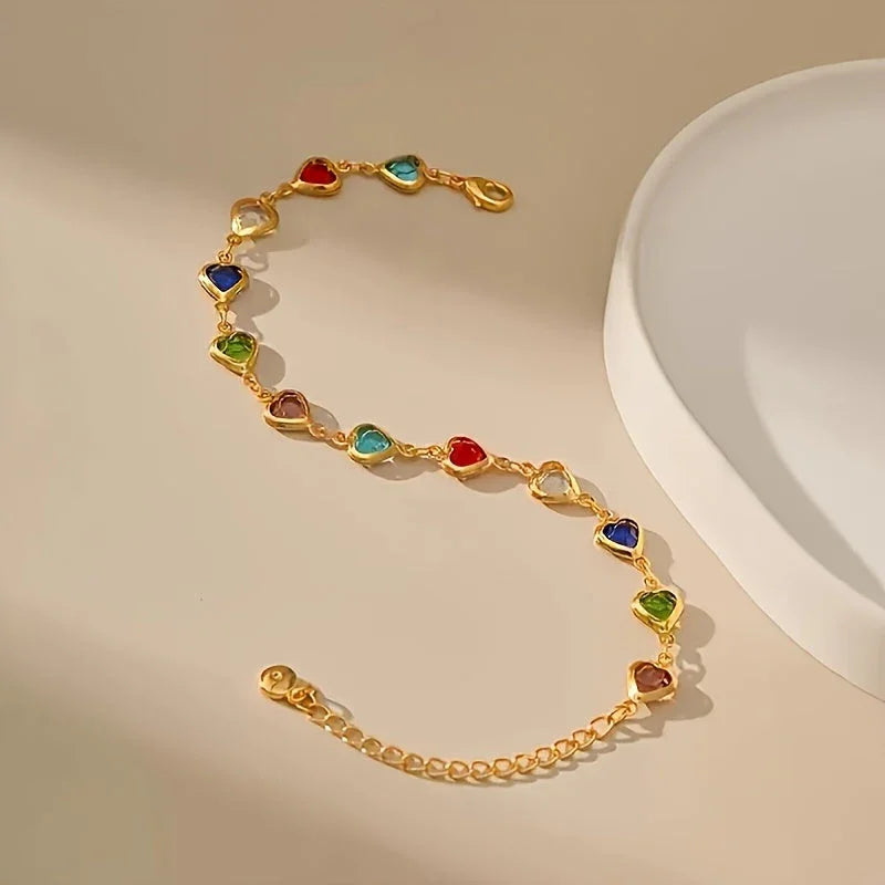 Gold-tone heart charm bracelet with multicolor enamel heart stones, flat lay