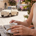 Solitaire ring with small round gemstone on hand holding a cup