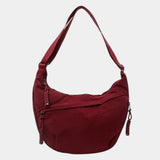 Burgundy anti-theft crossbody bag with curved hobo shape, adjustable strap, and zipper pull.