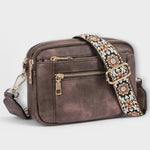 Dark brown small crossbody bag with flap front, front zipper, and patterned fabric strap.