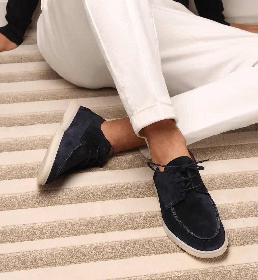 Navy blue suede lace-up loafers on feet with white pants