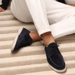 Navy blue suede lace-up loafers on feet with white pants