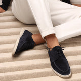 Navy blue suede lace-up loafers on feet with white pants